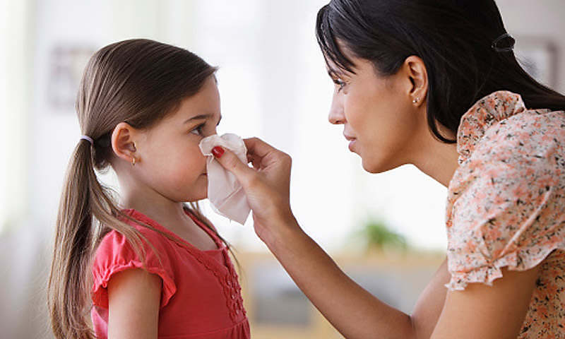 Mother wiping nose of daughter with tissue